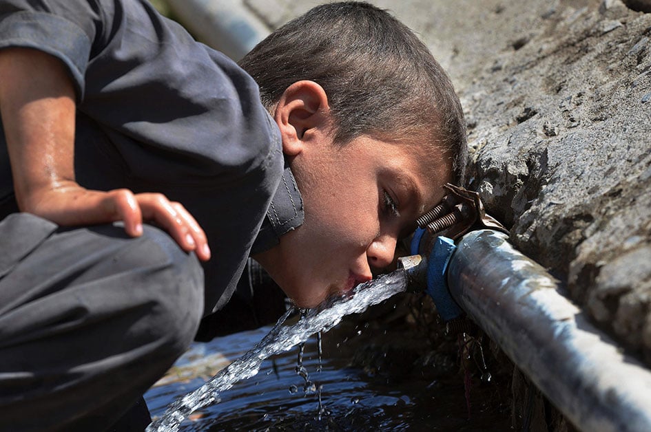 A small child drinking water straight from the pipe