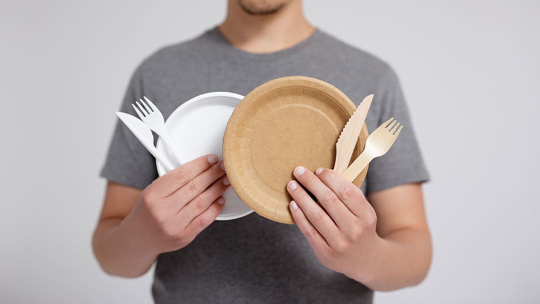 A man holding bioplastic and conventional plastic plates and cutlery